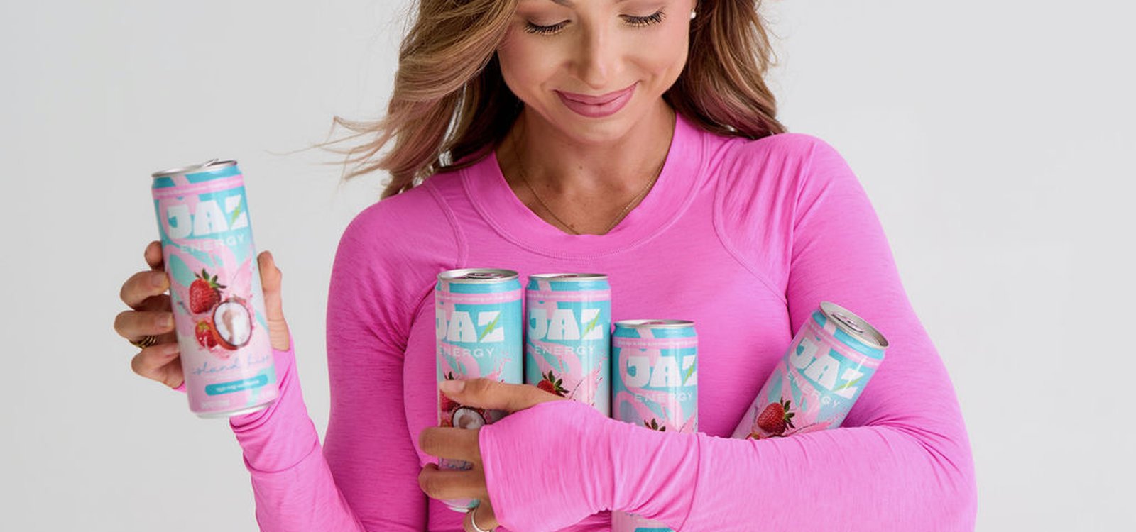 Woman in pink shirt holding multiple Jaz Energy cans – clean energy drinks with natural caffeine and no crash.